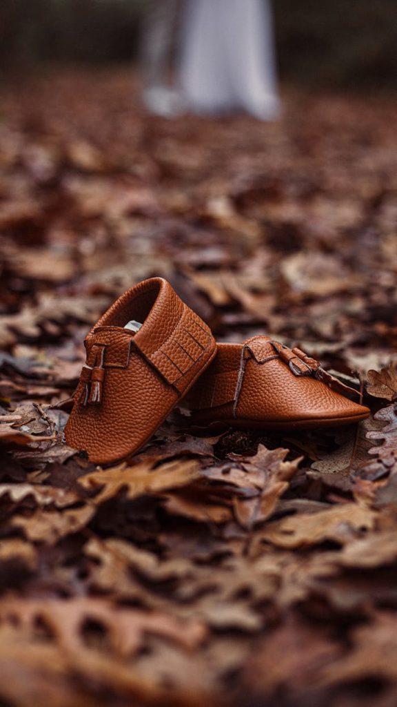 Brown baby shoes resting on a bed of fall leaves, capturing the essence of autumn.