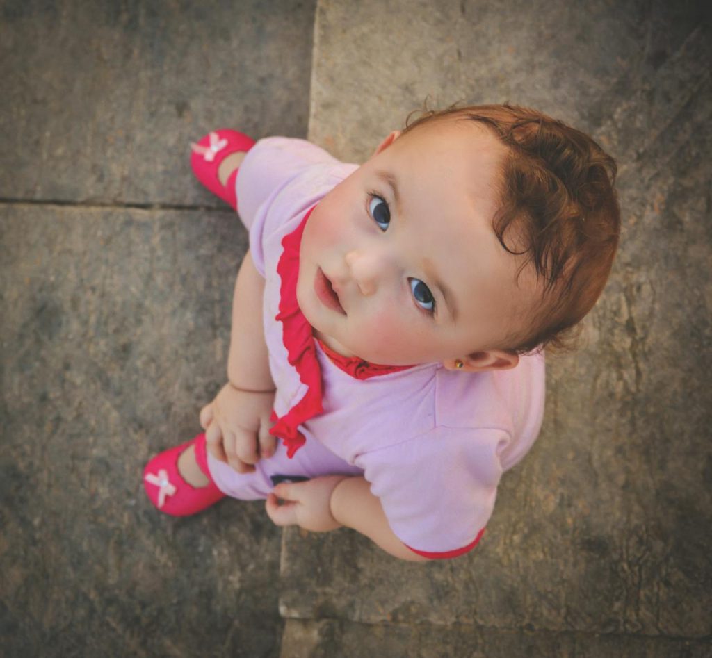 Cute toddler wearing pink, captured from above, gazing up with innocence and curiosity