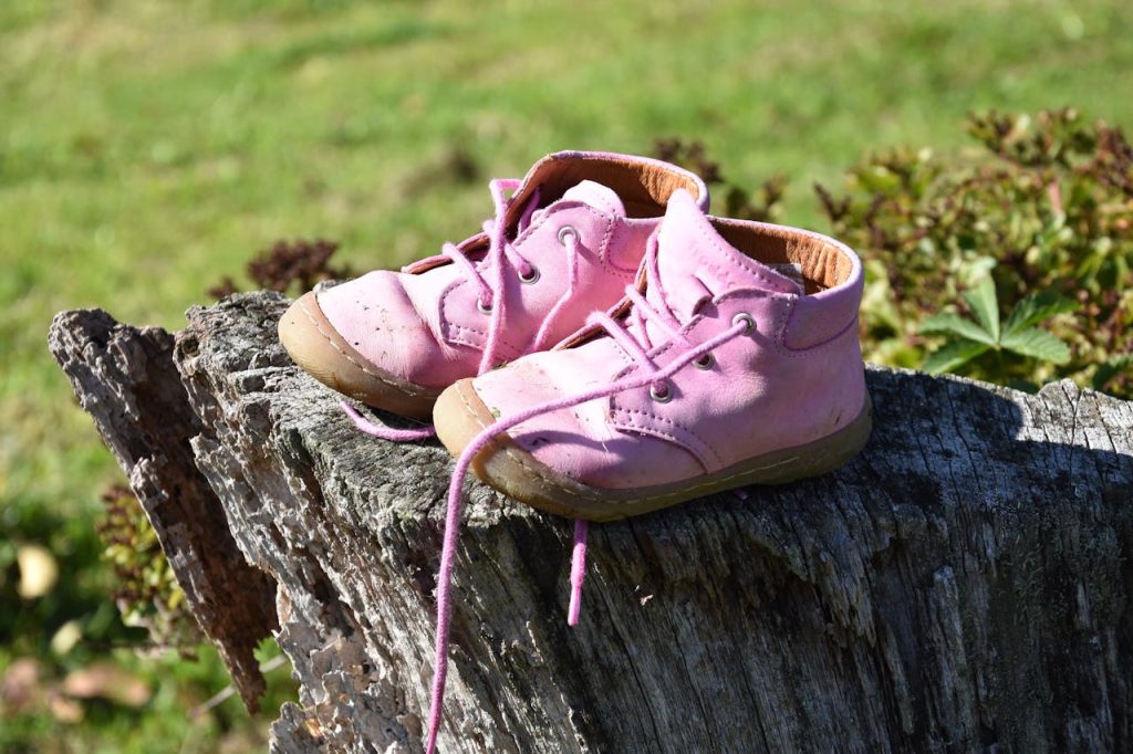 Close-up of pink baby shoes on a tree stump in a grassy area, capturing a rustic outdoor feel.